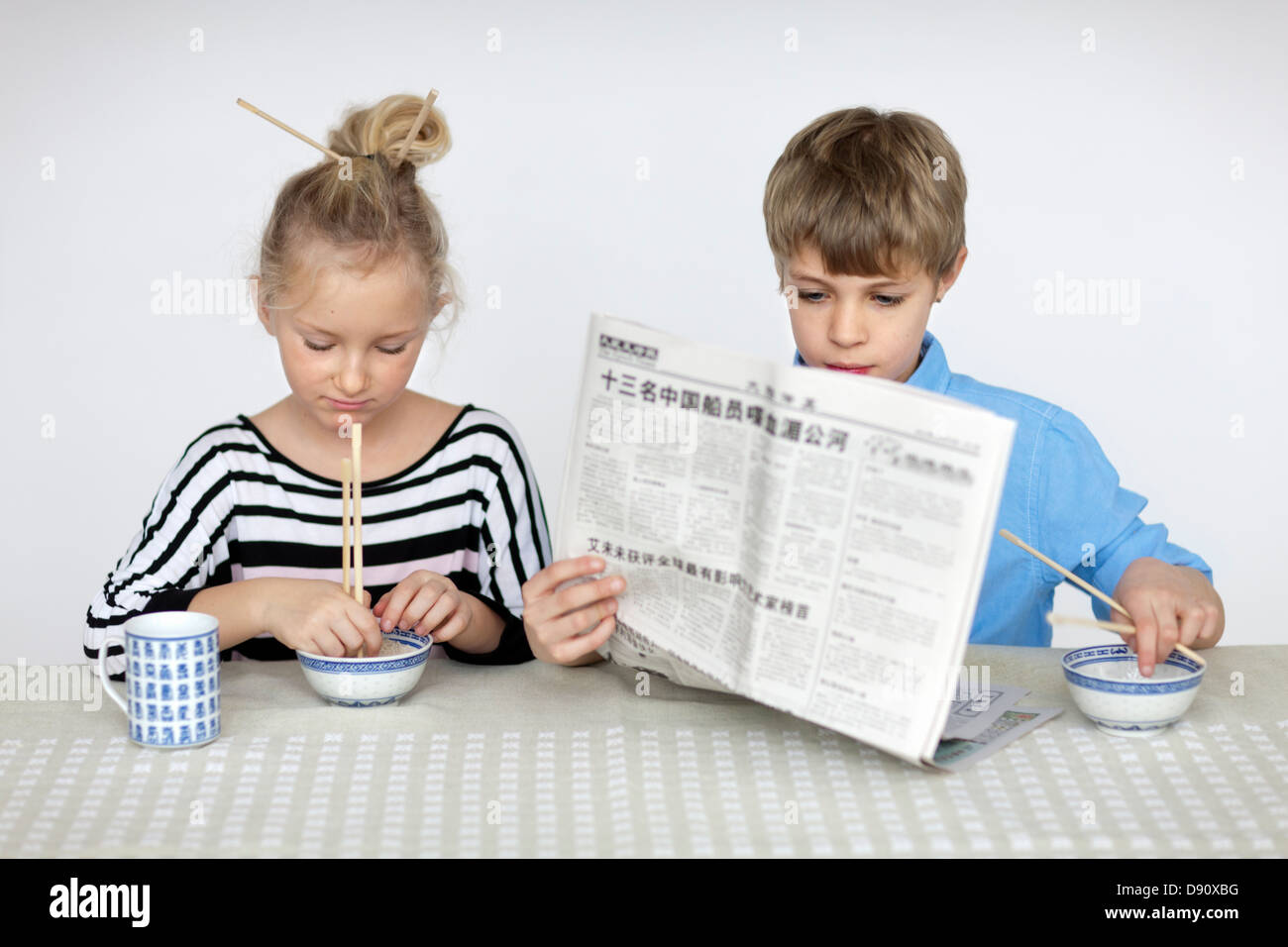 Mädchen, Essen mit Stäbchen und junge liest Zeitung Stockfoto