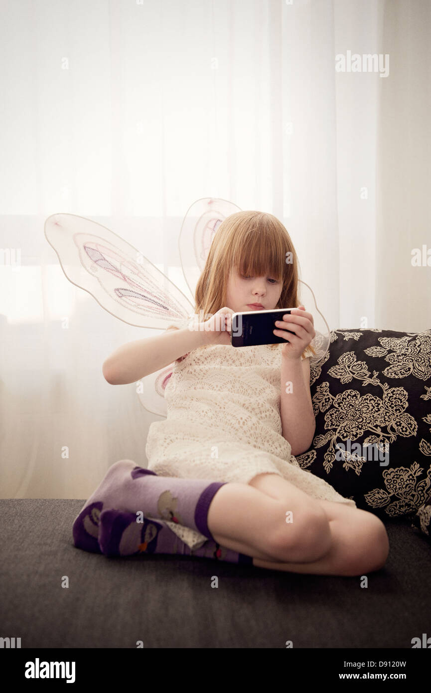Mädchen tragen Feenflügel mit Handy spielen Stockfoto