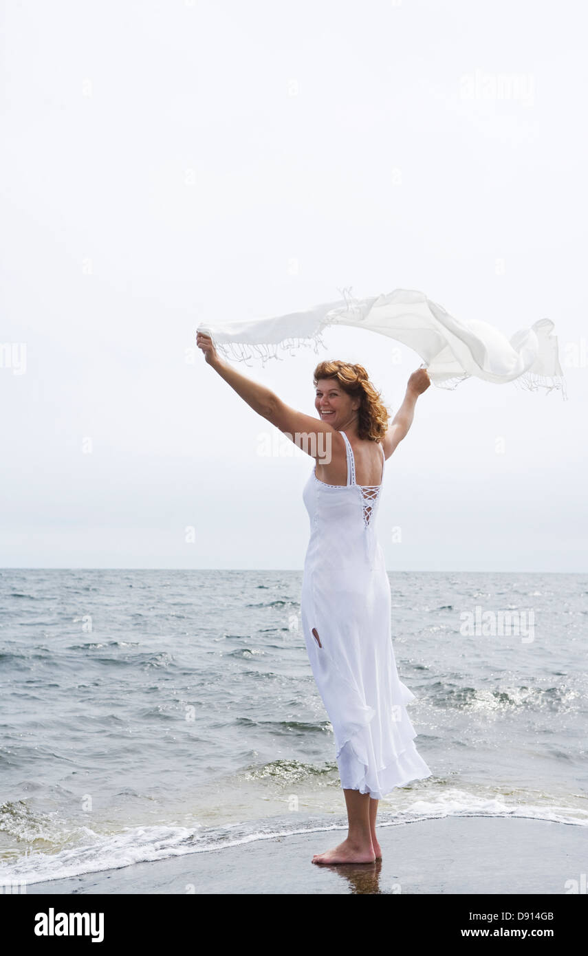 Eine Frau hält einen weißen Schal im Wind am Meer, Schweden. Stockfoto