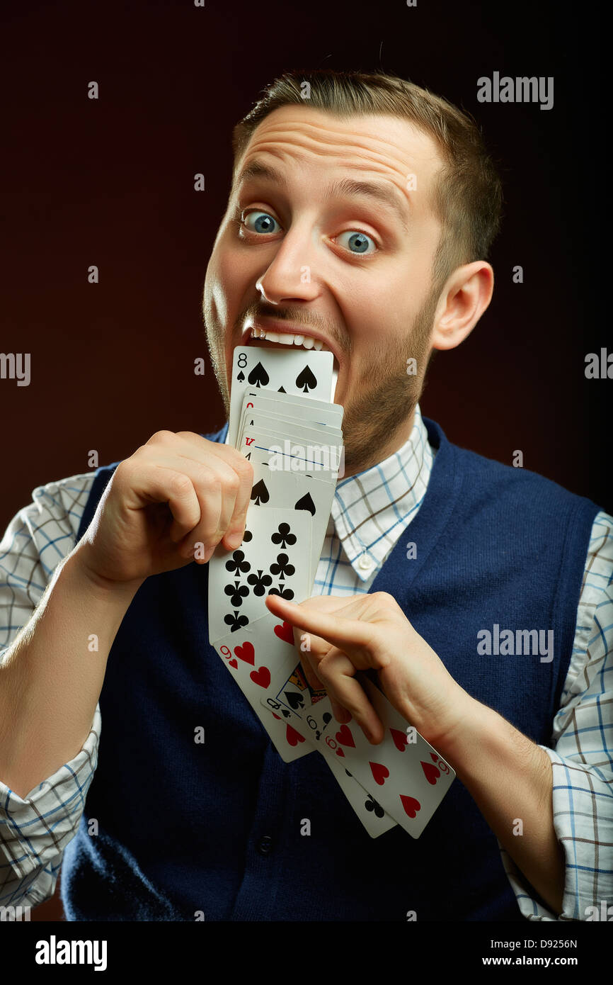 Fröhliche lustige männliche Zauberer zieht aus seinem Mund eine Reihe von Spielkarten über dunklen Hintergrund. Stockfoto