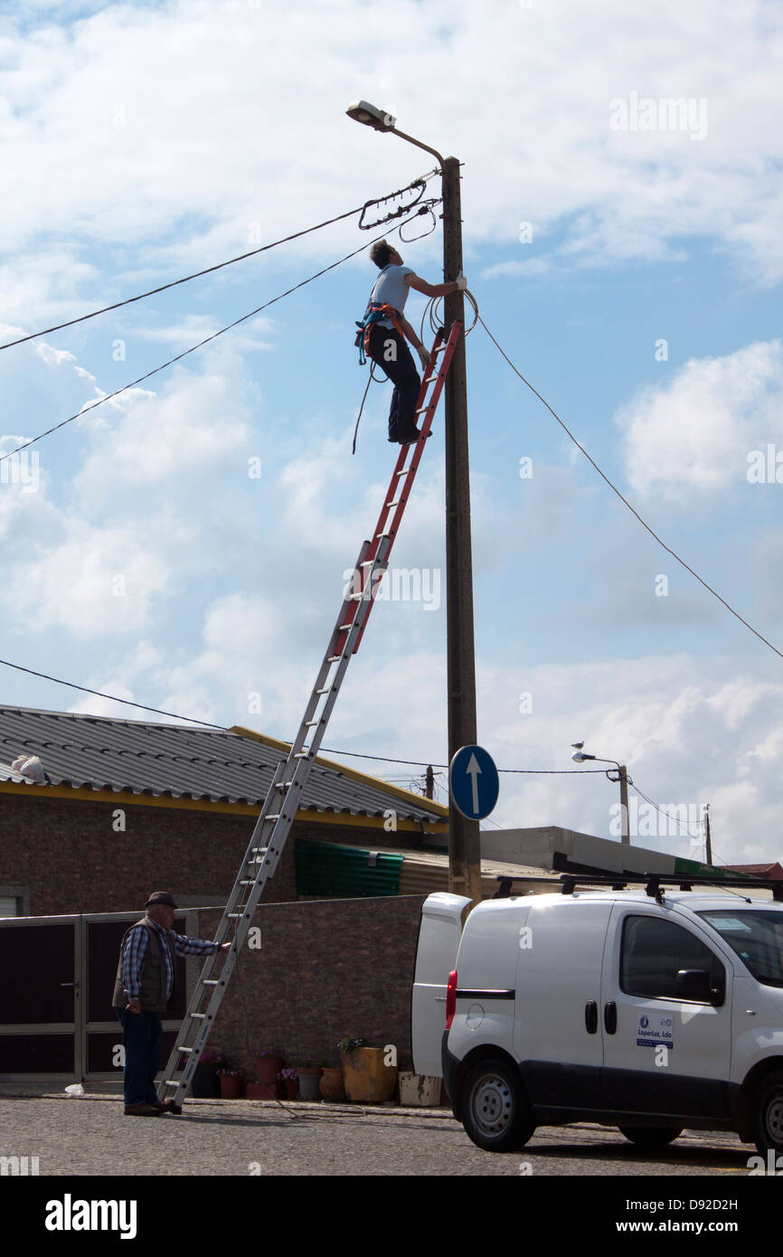 Strom die Firma einen Beitrag zu klettern, während der andere Mann die Treppe hält Stockfoto