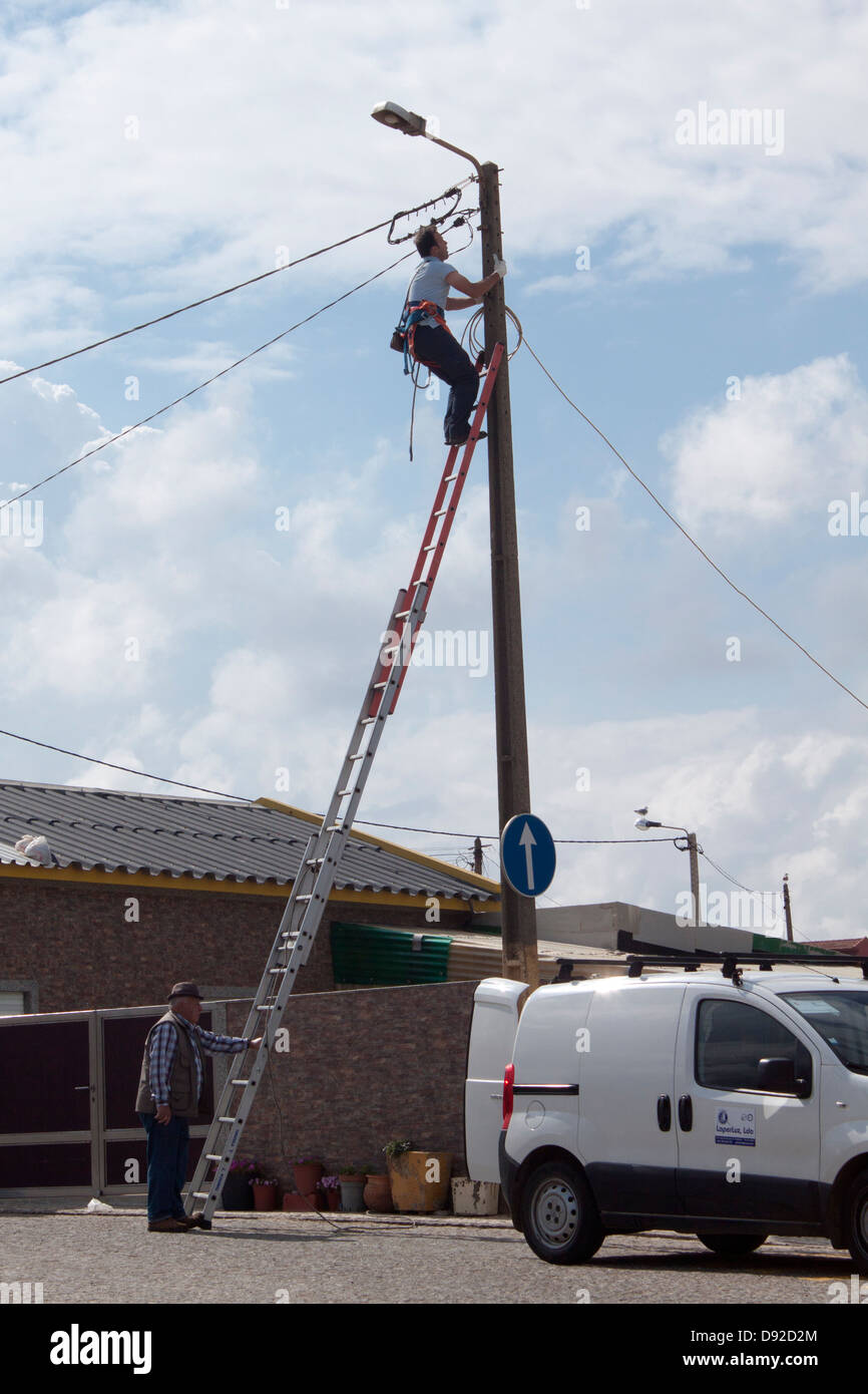 Strom die Firma einen Beitrag zu klettern, während der andere Mann die Treppe hält Stockfoto