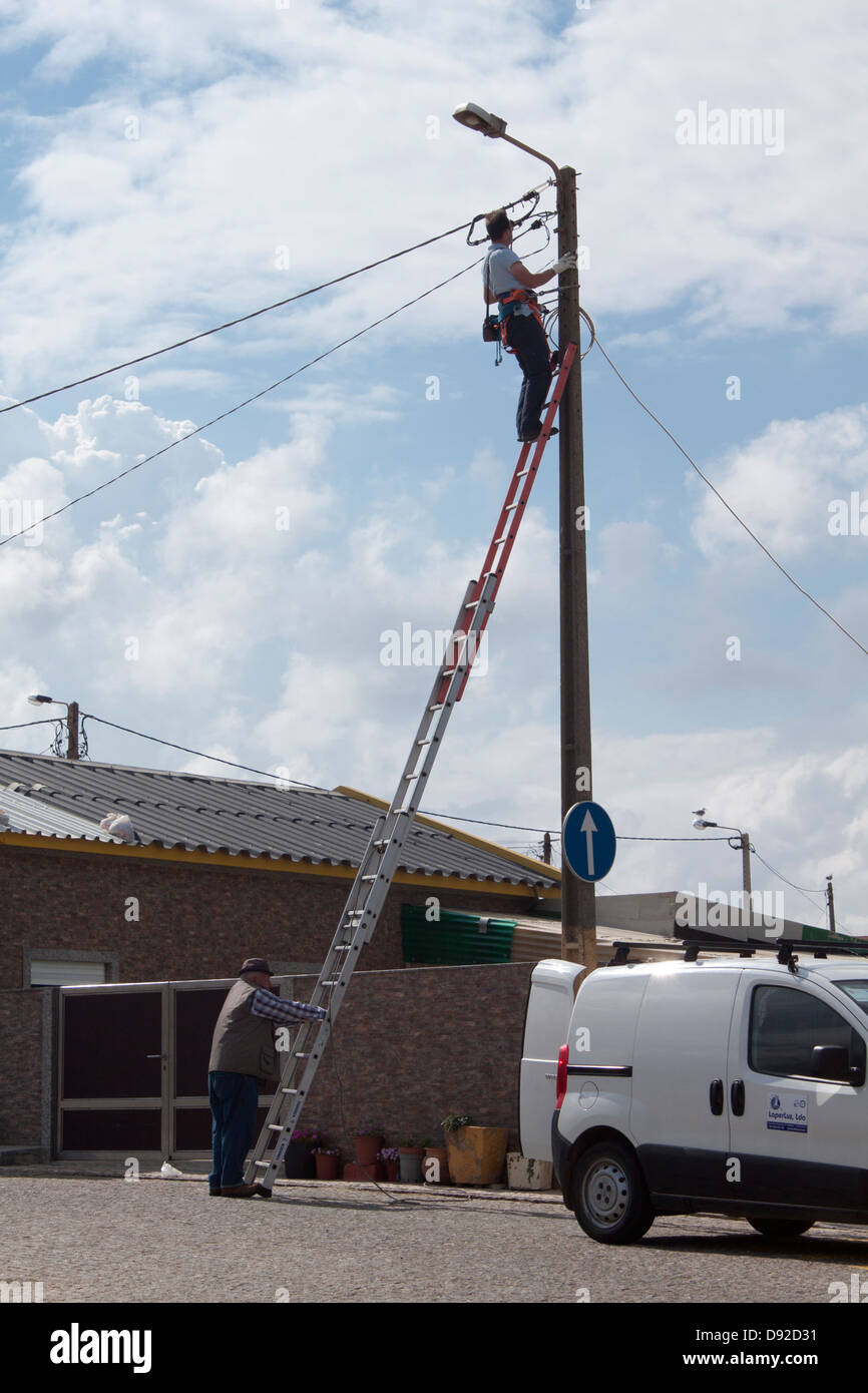 Strom die Firma einen Beitrag zu klettern, während der andere Mann die Treppe hält Stockfoto