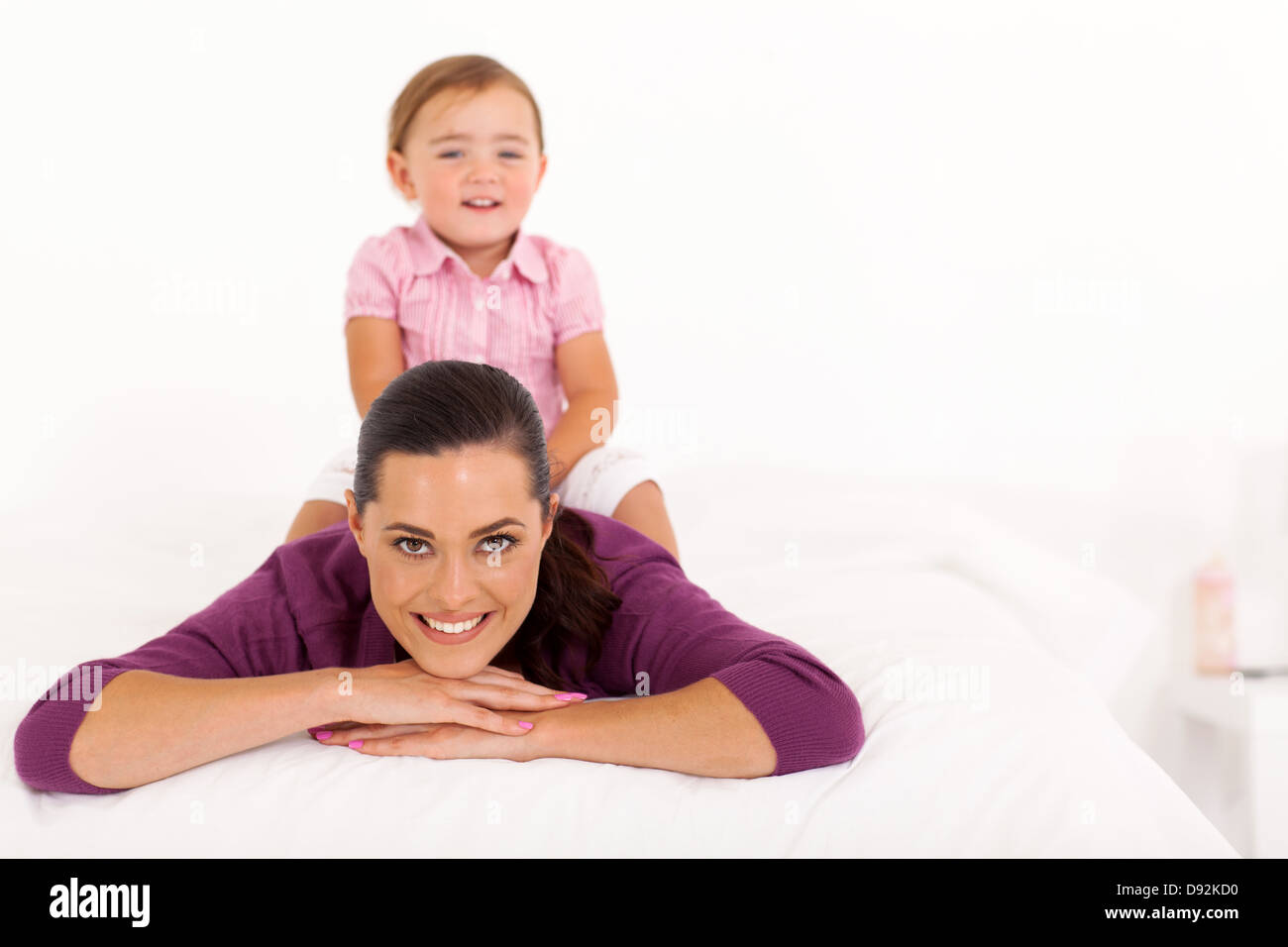 glückliche kleine Mädchen sitzen auf Mutter zurück auf Bett Stockfoto