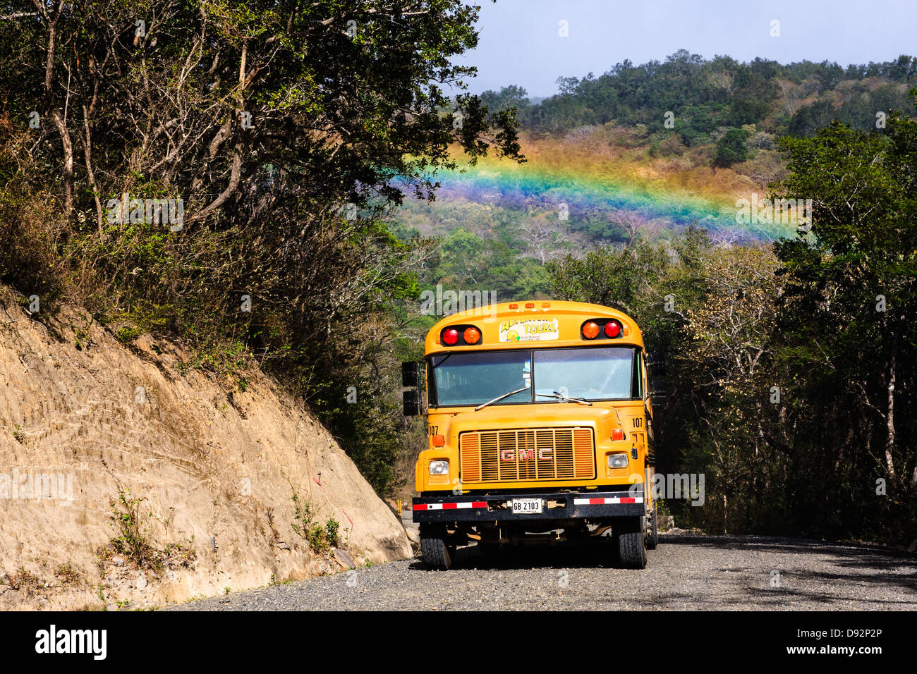 Ein gelber Bus unterquert ein Regenbogen in Costa Rica Stockfoto