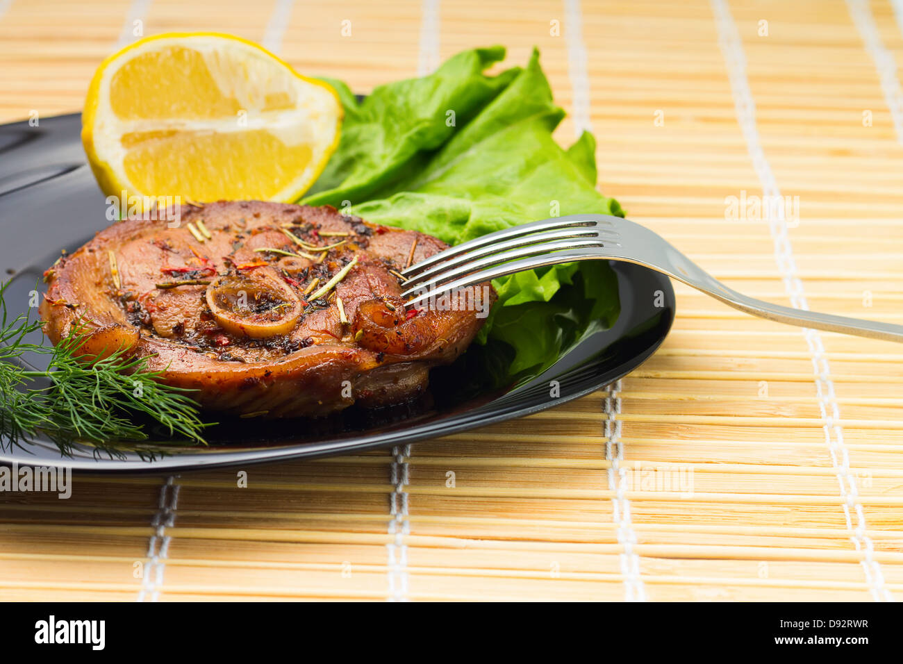 Gegrilltes Steak, Salat und Zitrone mit Gabel auf Bambus-Hintergrund Stockfoto