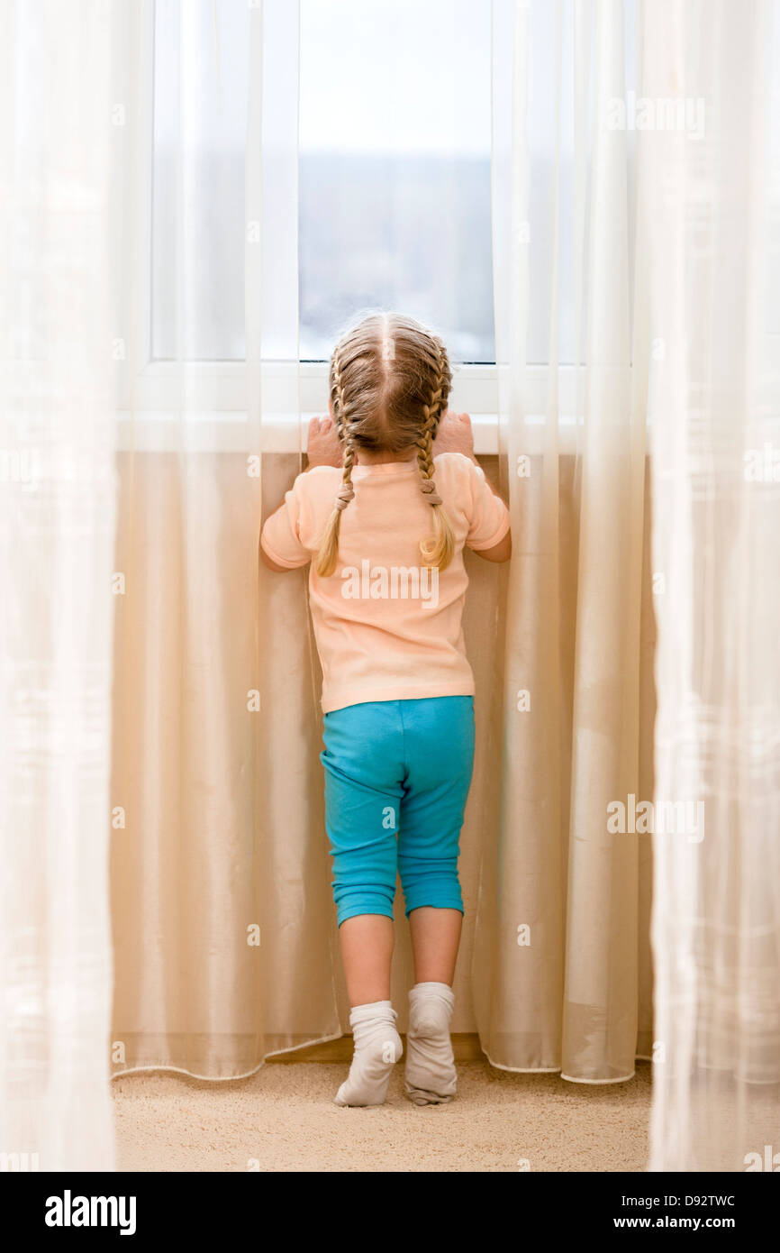 Kleines Mädchen auf ihren Zehenspitzen aus Fenster sehen wollen Stockfoto