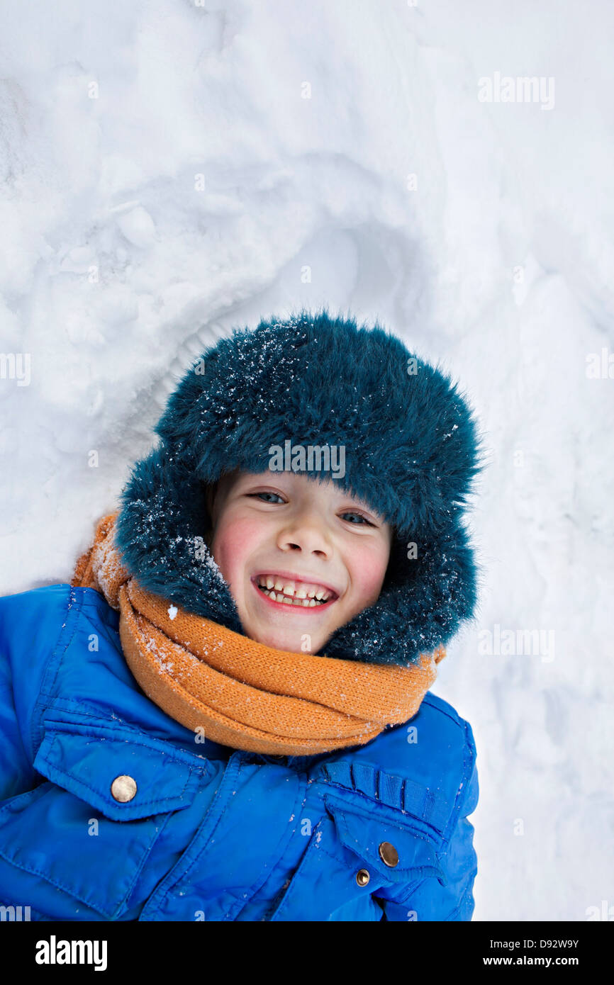 Ein fröhlicher Junge tragen warme Kleidung im Freien im Schnee liegen Stockfoto