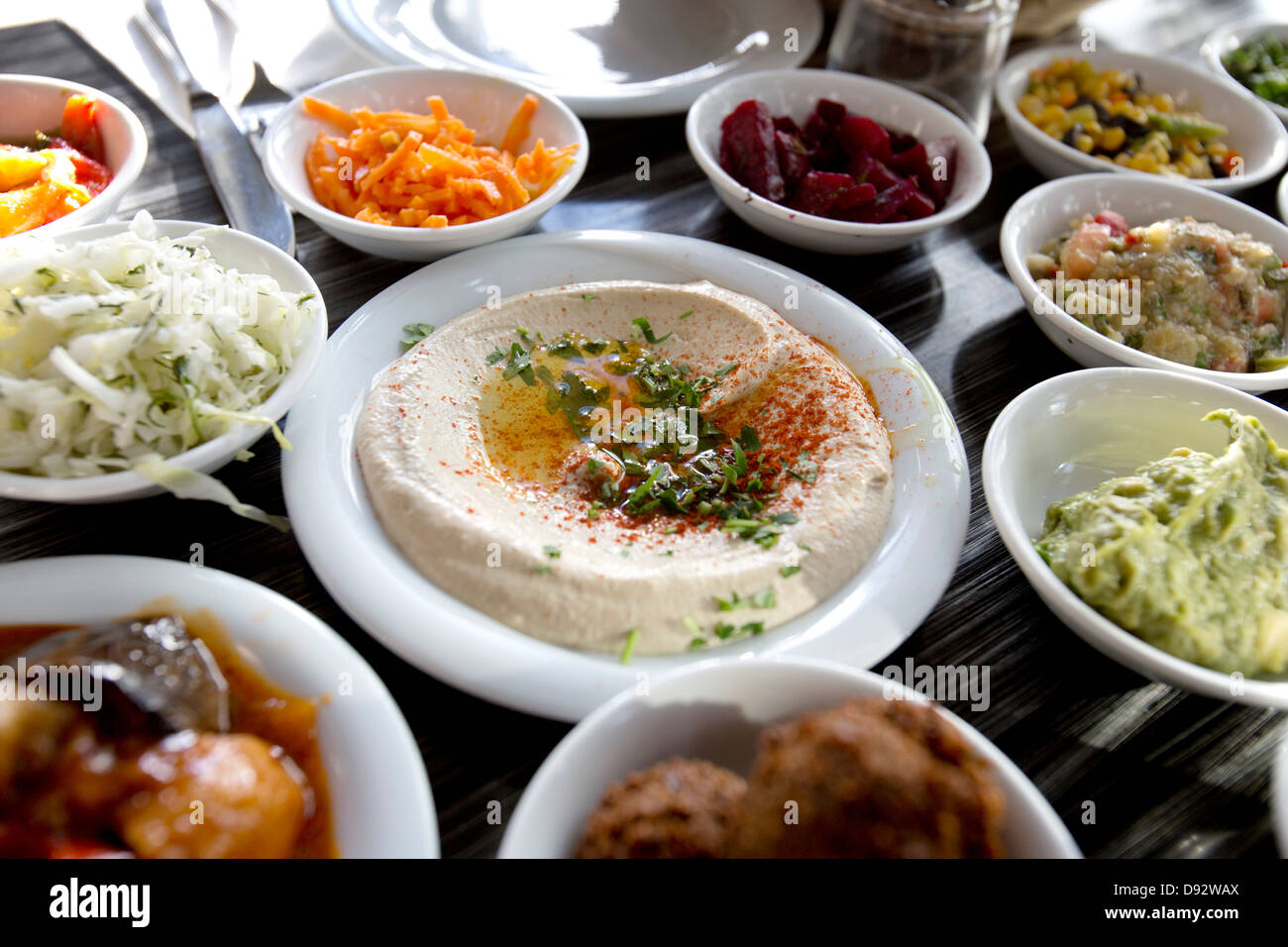 Einen Teller garniert Hummus auf Tisch, umgeben von verschiedenen Salaten Stockfoto