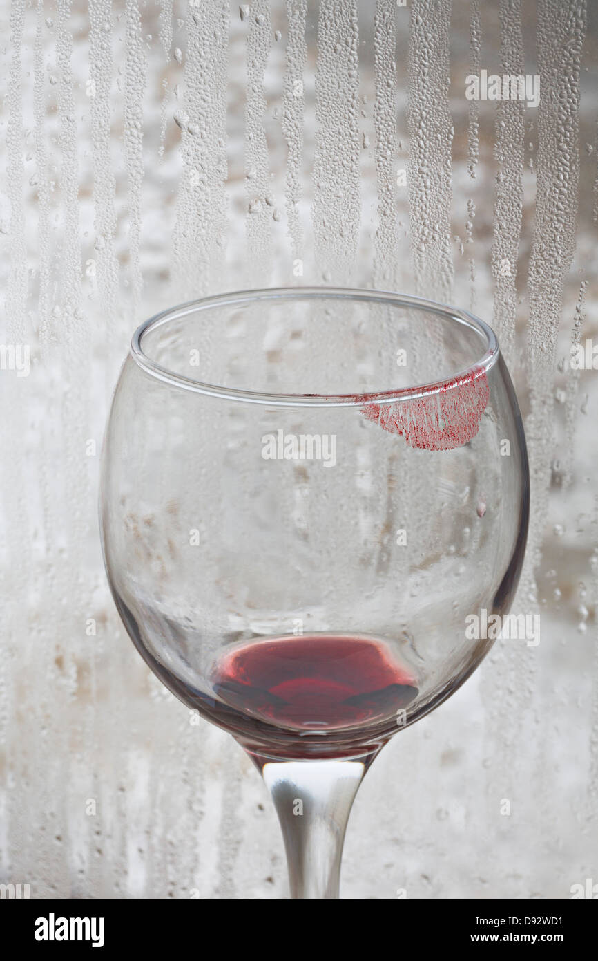 Lippenstift auf ein Glas Rotwein mit regen bedeckt Fenster im Hintergrund Stockfoto