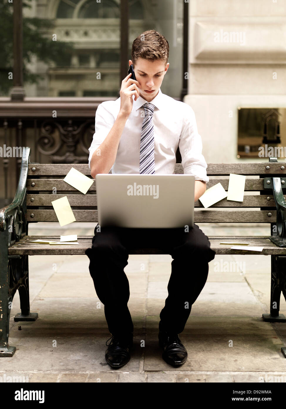 Geschäftsmann mit einem Smartphone während Sie einen Laptop verwenden und sitzen auf Bank mit Haftnotizen Stockfoto