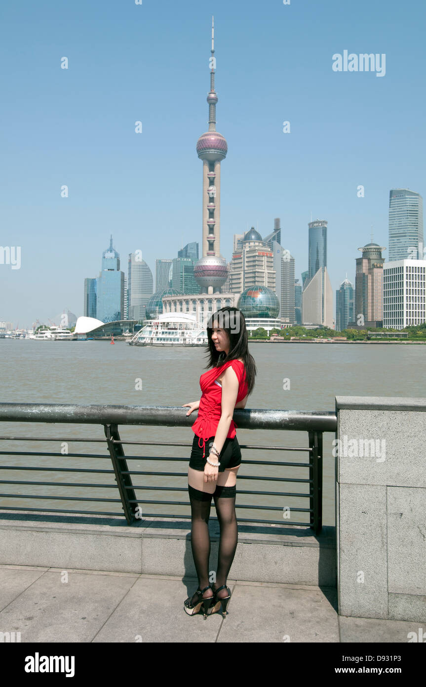 Eine junge Chinesin posiert für ein Foto auf den Bund mit der neuen Shanghai Pudong-Skyline im Hintergrund, Shanghai, China. Stockfoto
