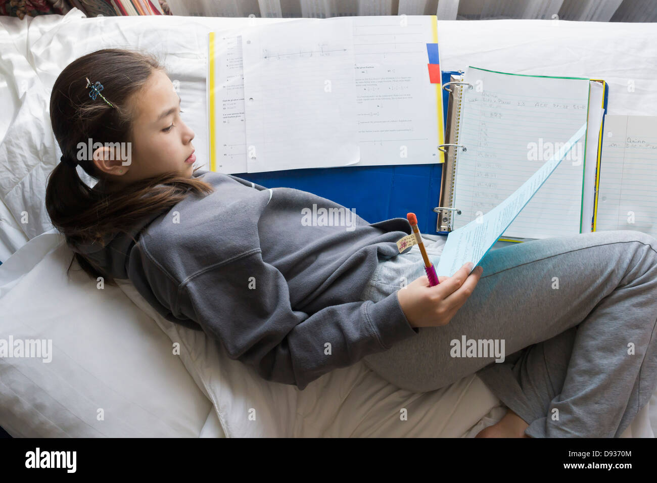 Gemischte Rassen Mädchen Hausaufgaben auf Bett Stockfoto