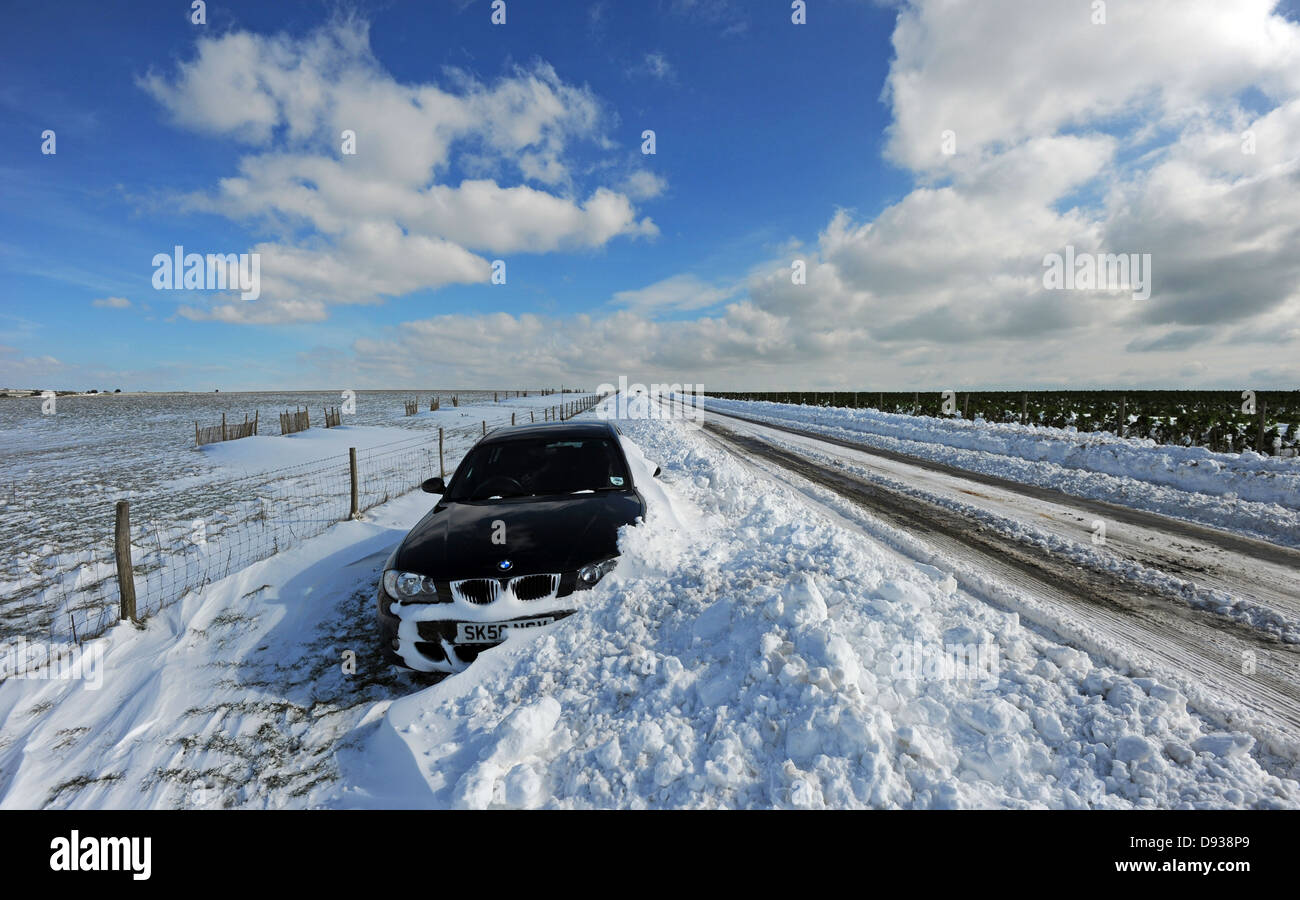 Ein BMW-Auto verlassen eine massive Schneeverwehungen auf eine Straße, die durch die Sussex Downs Stockfoto