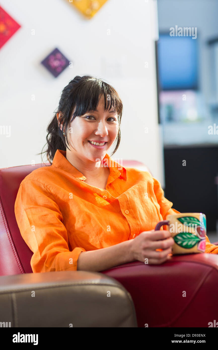 Asiatische Frau, die Tasse Kaffee im Sessel Stockfoto