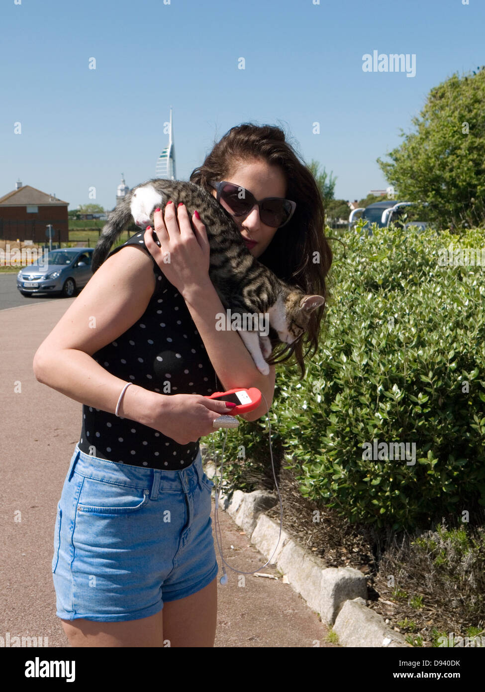 junge Frau in Sommerkleidung zu Fuß entlang der Strandpromenade mit Kätzchen auf die Schulter Stockfoto