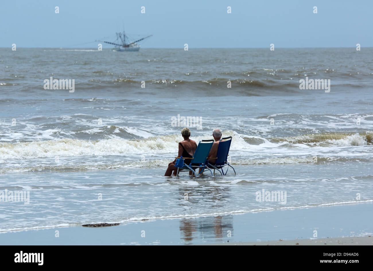 Älteres Ehepaar sitzen auf Stühlen in der Brandung am Strand, Hunting Island, South Carolina Stockfoto