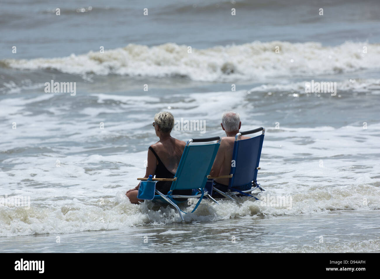 Älteres Ehepaar sitzen auf Stühlen in der Brandung am Strand, Hunting Island, South Carolina Stockfoto