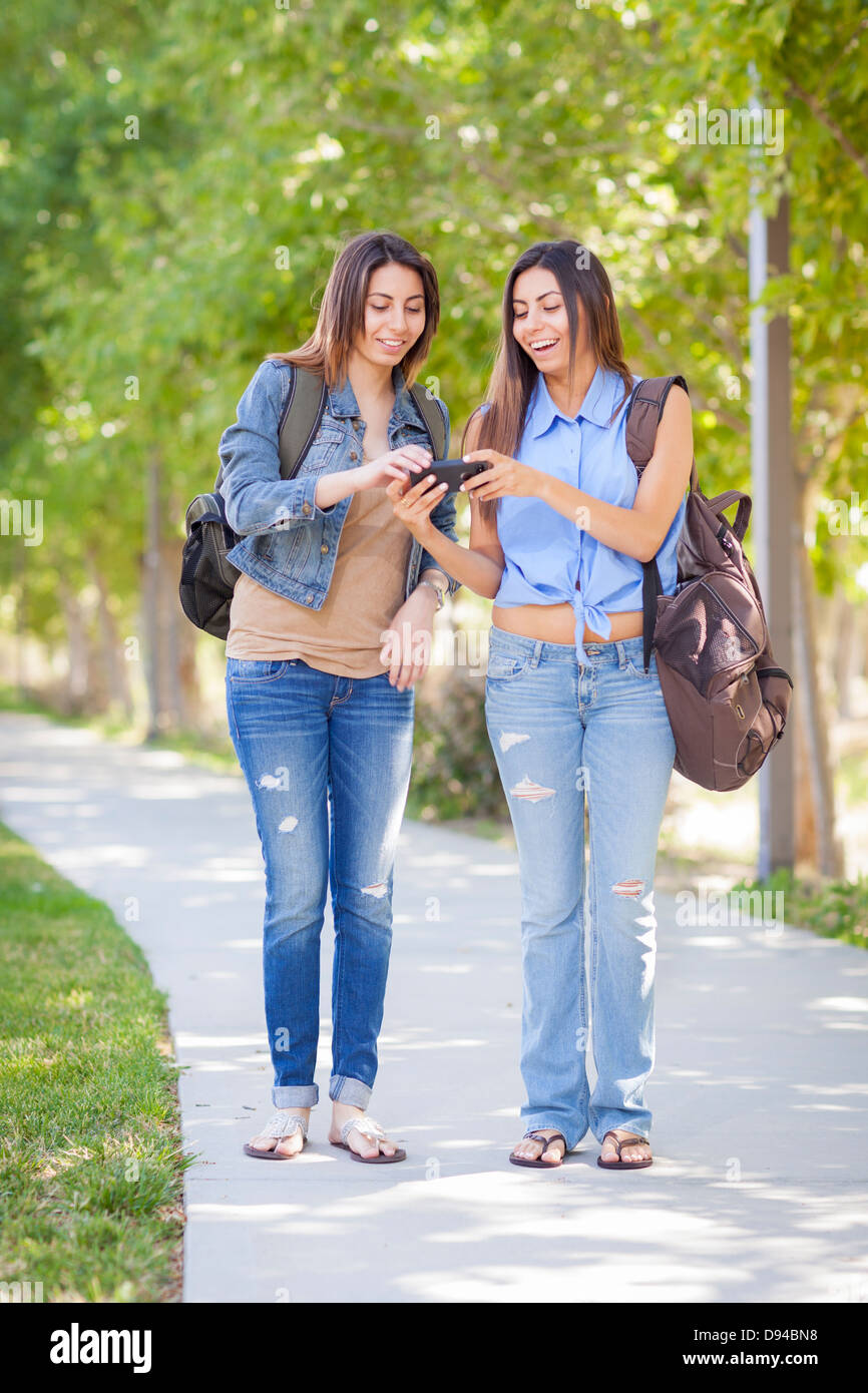 Junger Erwachsener gemischt Rennen Zwillingsschwestern teilen Handy Erfahrung außerhalb. Stockfoto