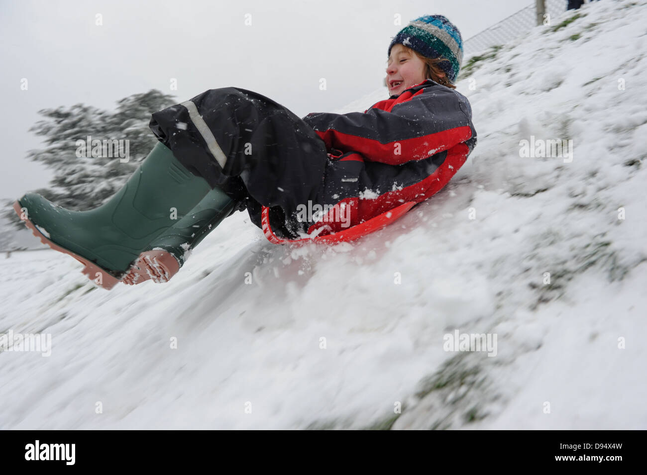 ein kleiner junge Spaß schiebt einen verschneiten Hang hinunter auf einem Schlitten im Schnee Stockfoto
