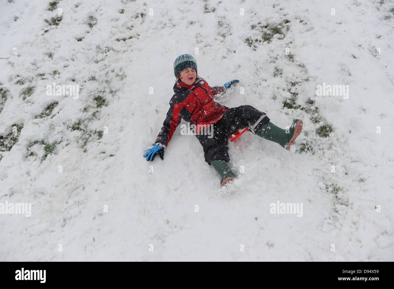 Ein Junge Spaß und rutschen nach unten einen verschneiten Hang auf einem Schlitten Stockfoto