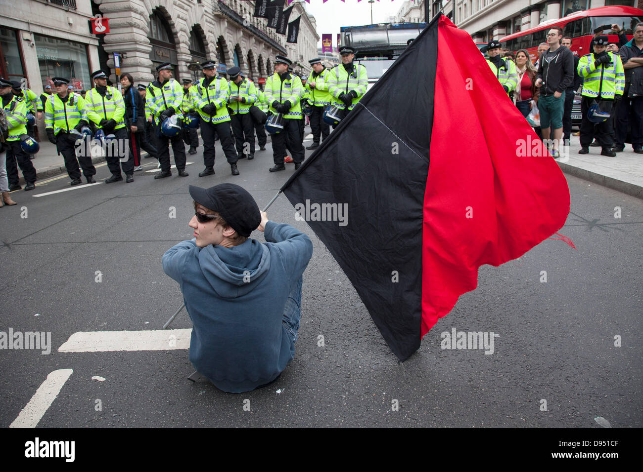 Demonstrant setzt sich auf der Straße mit einem schwarzen und roten anti-kapitalistischen Flagge vor Polizeilinien während der Demonstration gegen den bevorstehenden G8-Gipfel in central London, UK. Stockfoto