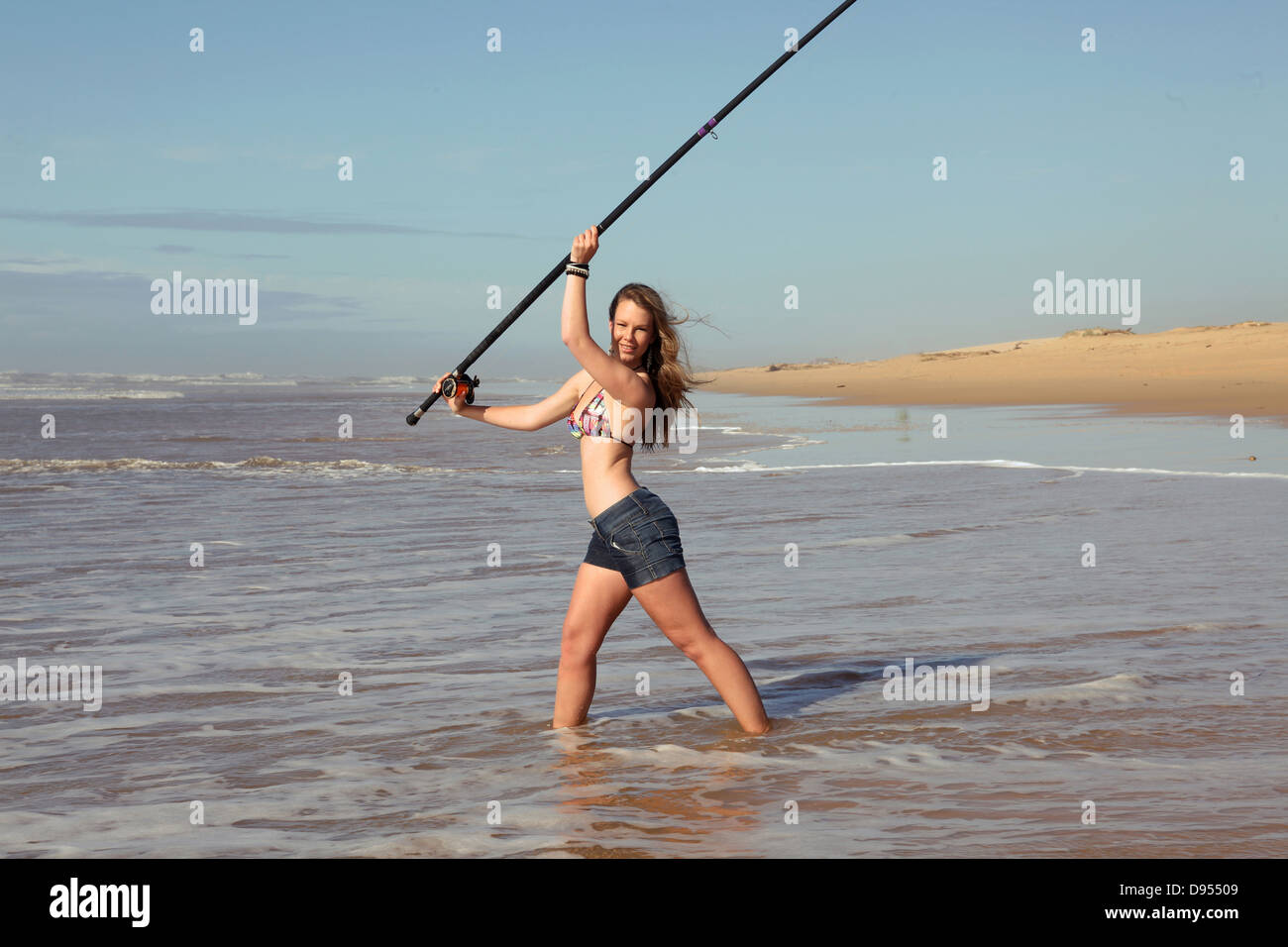 eine sexy junge Dame im Bikini wirft Haaransatz versucht, einen Fisch im Meer zu fangen. Stockfoto