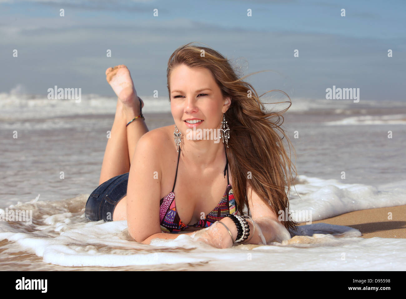 Eine junge sexy blonde Lady in ihrem Bikini in den brechenden Wellen am Strand liegen und lächelnd Weg. Stockfoto