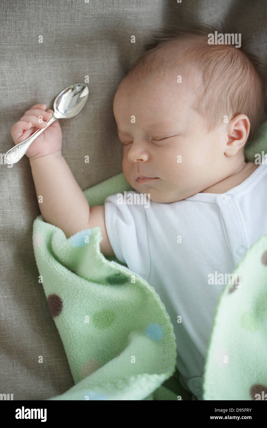 Neugeborenes Babymädchen in einem weißen Unterhemd auf ein Bett mit einem silbernen Löffel in der Hand, Ontario, Kanada Stockfoto