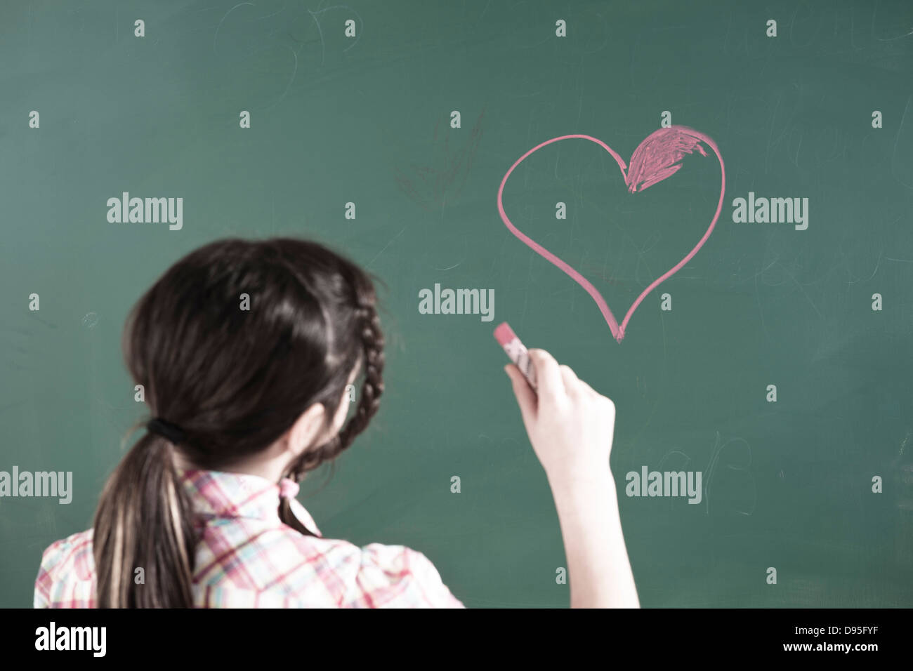 Mädchen Zeichnung Herz an Tafel im Klassenzimmer Stockfoto