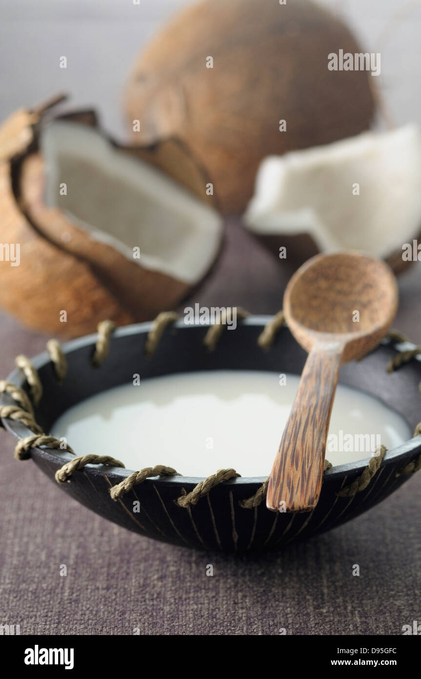 Kokos-Milch in Schüssel mit einem Holzlöffel, Kokosnüsse im Hintergrund Stockfoto