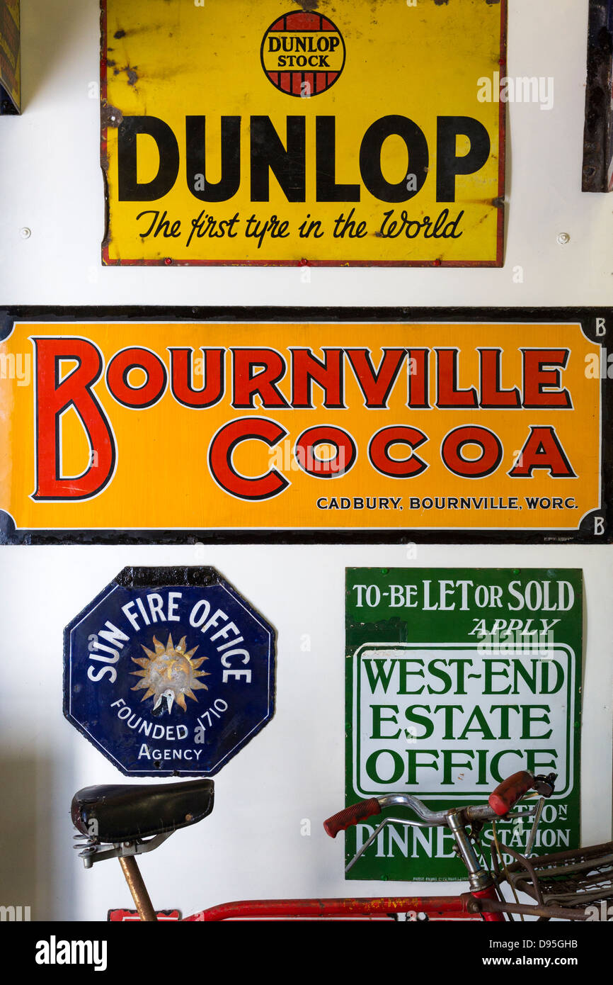 Fahrrad, lehnte sich gegen eine Wand aus Blech Emailleschilder Werbung Dunlop, Bournville, Sun Fire und West-End-Immobilien-Büro. Stockfoto