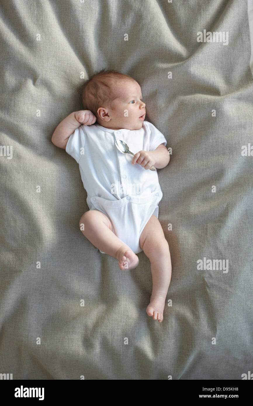 Neugeborenes Babymädchen in einem weißen Unterhemd auf ein Bett mit einem silbernen Löffel in der Hand, Ontario, Kanada Stockfoto