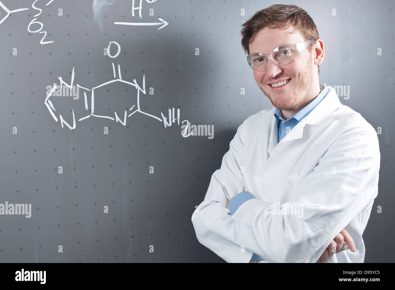 Deutschland, Porträt des jungen Wissenschaftlers stehen neben Reaktionsgleichung an Tafel, Lächeln Stockfoto