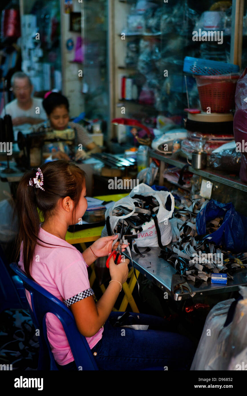 Familienwerkstatt mit Erwachsenen auf Nähmaschinen und junge Mädchen schneiden Stoff in Bangkok, Thailand Stockfoto