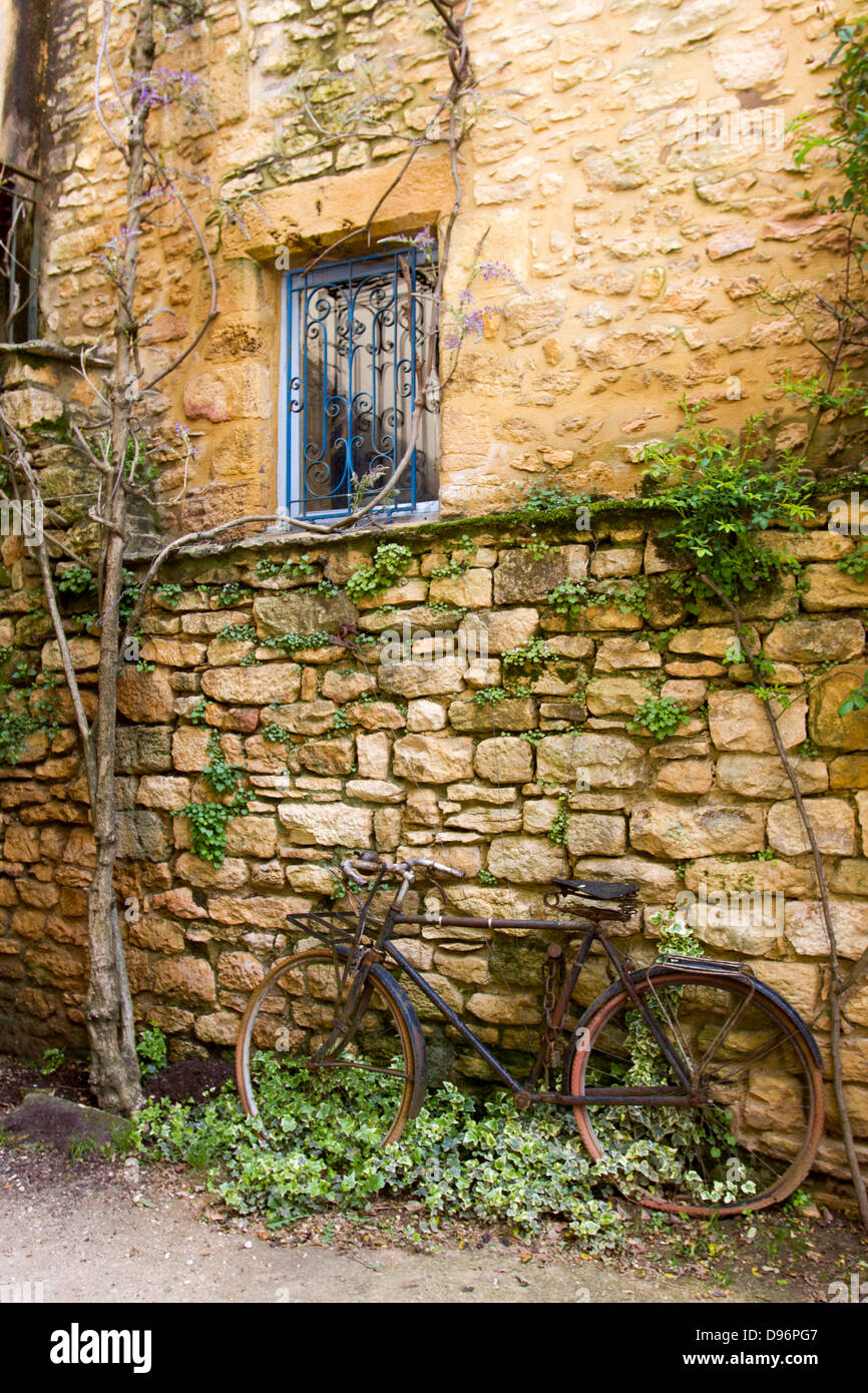 Rostigen Fahrrad gelehnt alte Steinmauer mit Reben unter schmiedeeisernen Fenster in Sarlat, Dordogne Region Frankreichs Stockfoto