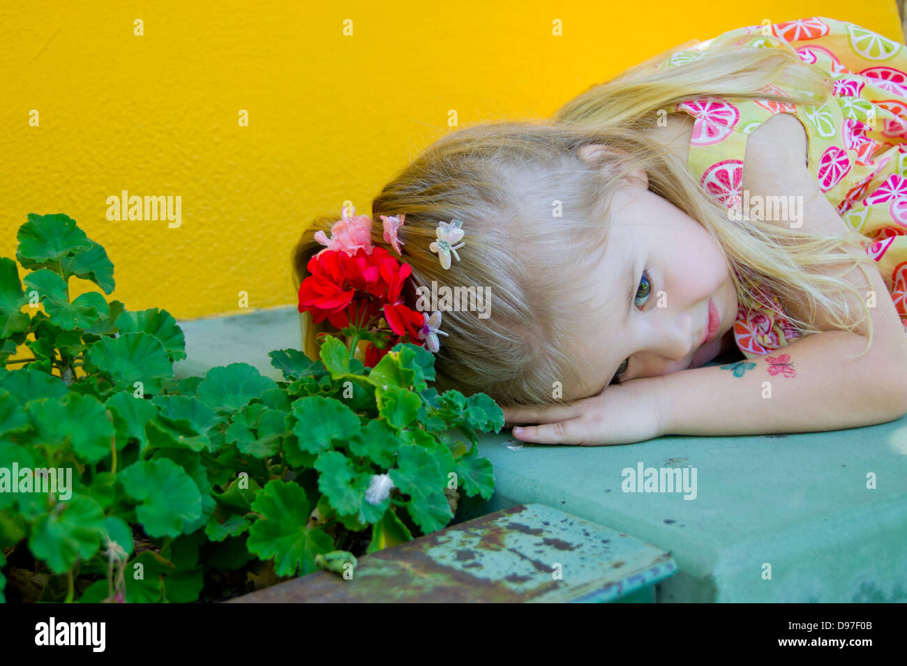 Ein drei Jahres altes Mädchen hängt den Kopf eine alte blau lackierten Bank in der Nähe von roten Blüten. Stockfoto