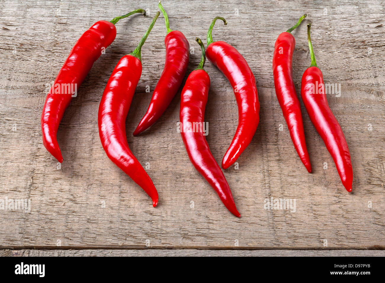Rote Chilis auf rustikalen Hintergrund - sieben rote Chilischoten auf einem Brett oder rustikalen Hintergrund. Stockfoto
