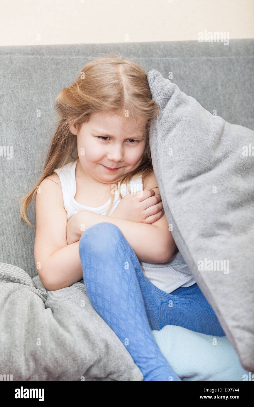 Beleidigt kaukasische Mädchen versteckt sich hinter einem Kissen auf der Couch. Ihre Arme gefaltet Stockfoto