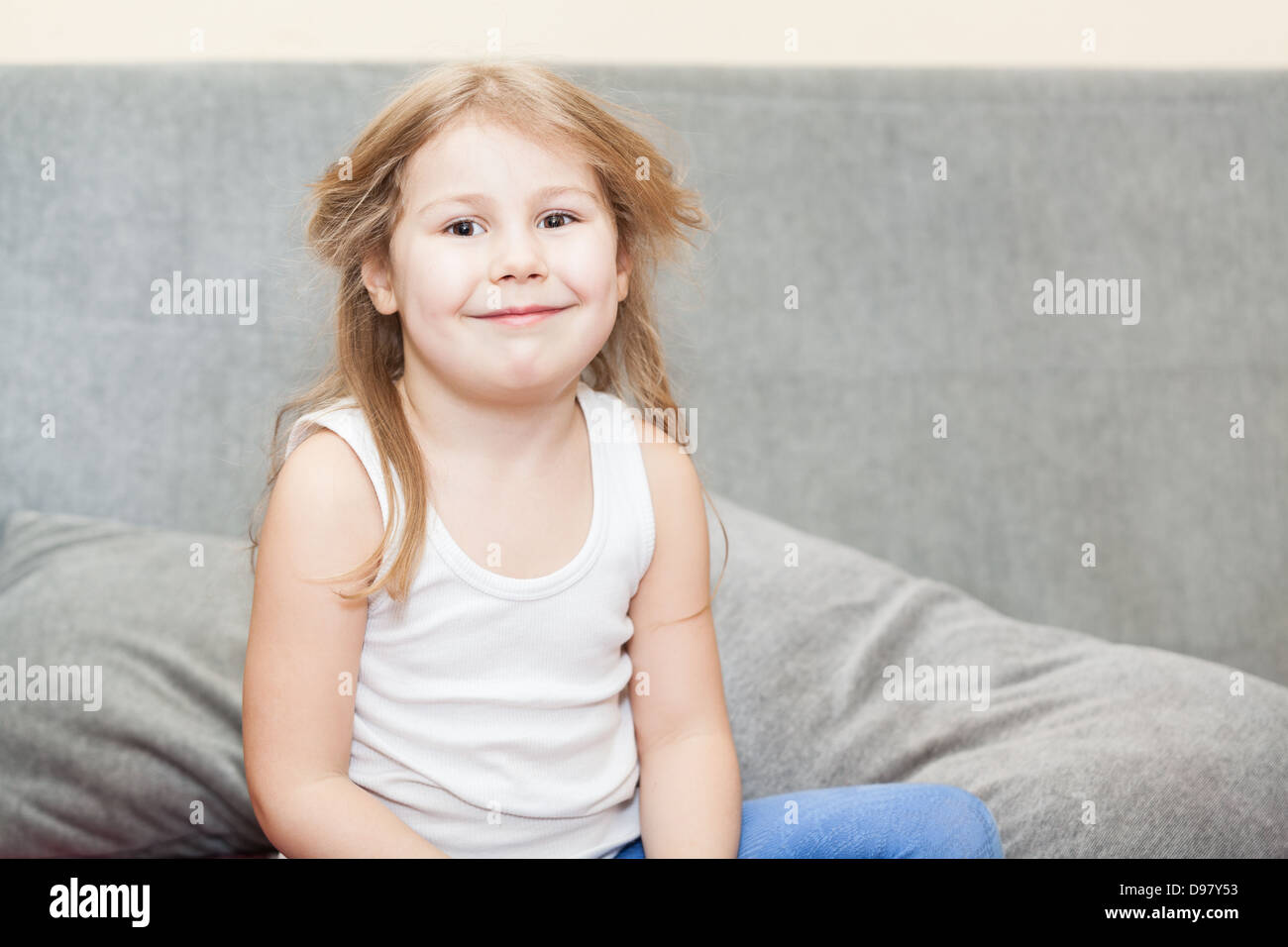 Wenig kaukasische Mädchen mit zerzausten Haaren sitzen auf der Couch mit einem listigen Grinsen Stockfoto