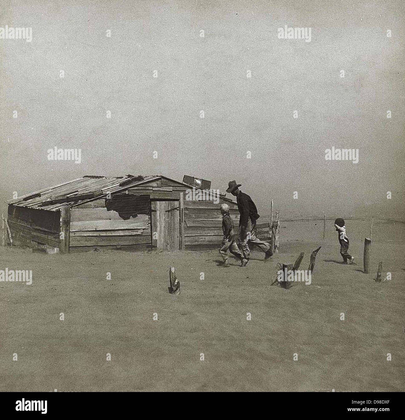 Sturm in der Dust Bowl, Amerika, um 1930. Und jungen Mann zu Fuß in Richtung Holzhütte schrittweise durch Wind geblasen Staub bedeckt. Kleiner Junge hält seine Hand sein Gesicht zu schützen. Stockfoto