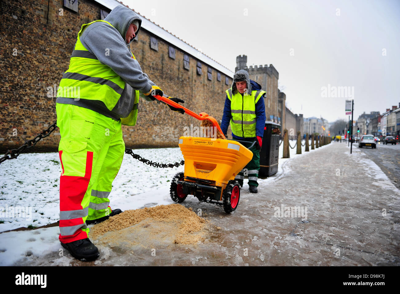 Des Rates Arbeiter mit Körnung zur Schneeräumung auf dem Bürgersteig vor Schloss von Cardiff, UK. Stockfoto