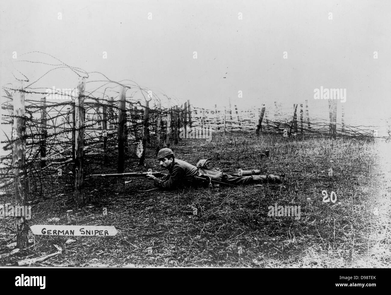 Der erste Weltkrieg 1914-1918: Deutsche Sniper trägt einen pickelhelm, liegen auf dem Boden hinter Stacheldraht Verstrickungen, das Gewehr bereit. Stockfoto
