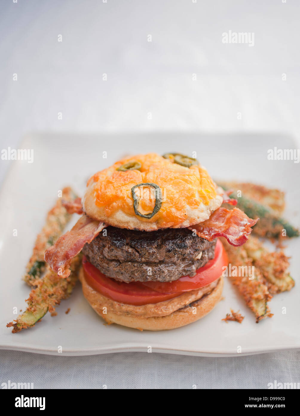 Burger Speck Tomaten Senf Jalapeño Käse Brötchen und Zucchini fries Stockfoto