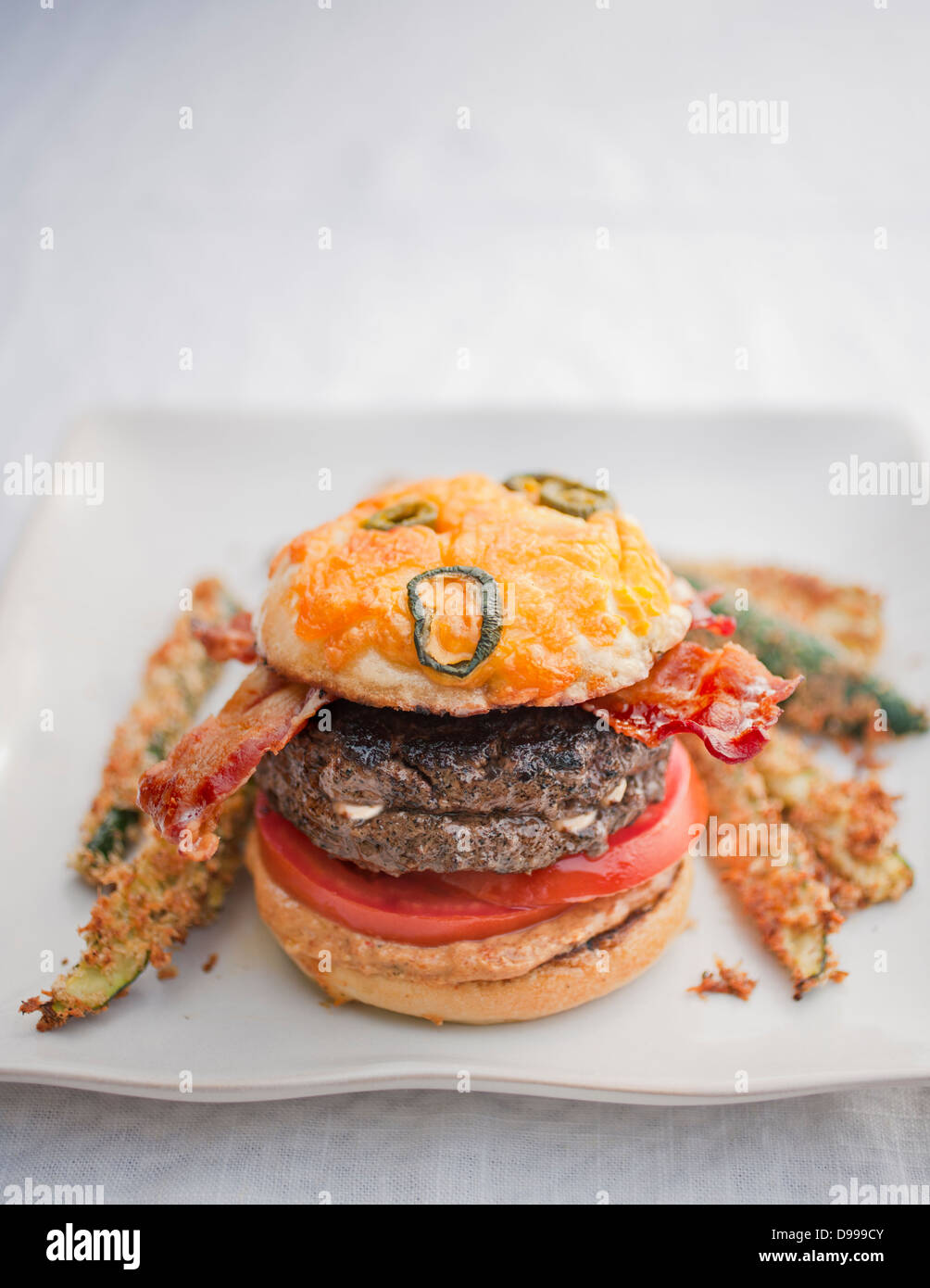 Burger Speck Tomaten Senf Jalapeño Käse Brötchen und Zucchini fries Stockfoto