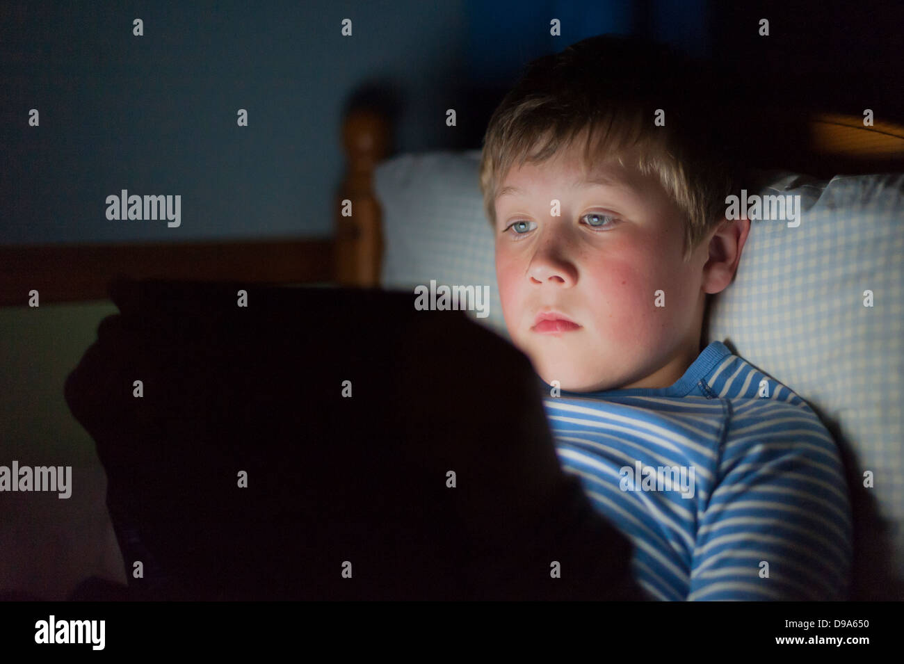 Ein 9-jähriger Junge mit einem Tablet auf das Internet im Bett Stockfoto