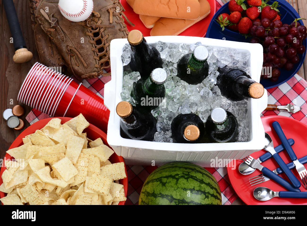 Draufsicht auf einem Picknick-Tisch mit Kühlbox voller Bier, Schüssel mit Chips, Wassermelone, Erdbeeren, Trauben, Mais-Chips. Stockfoto