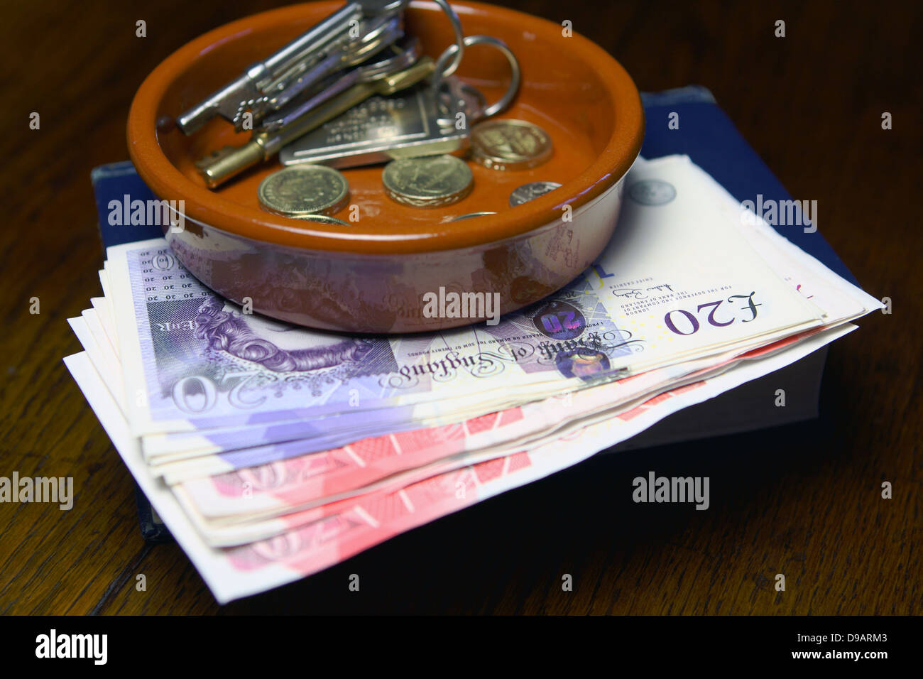 Eine braune Schale mit Sterling Münzen und Schlüssel ruht auf Sterling £50 und £20 Noten - alle auf ein Buch Stockfoto