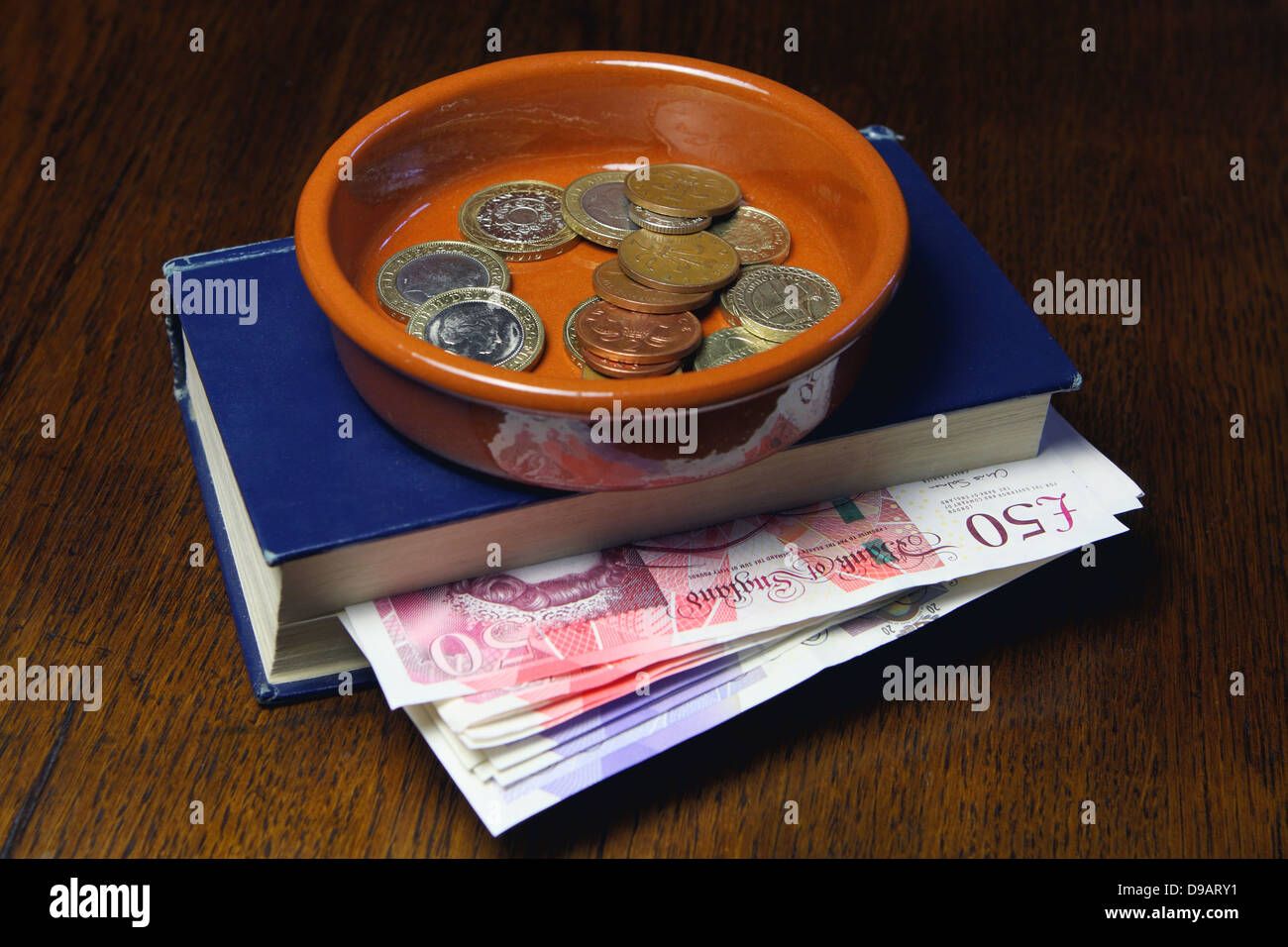 Eine braune Schale Containg Münzen auf ein Buch mit Sterling £50 und £20 Noten Stockfoto