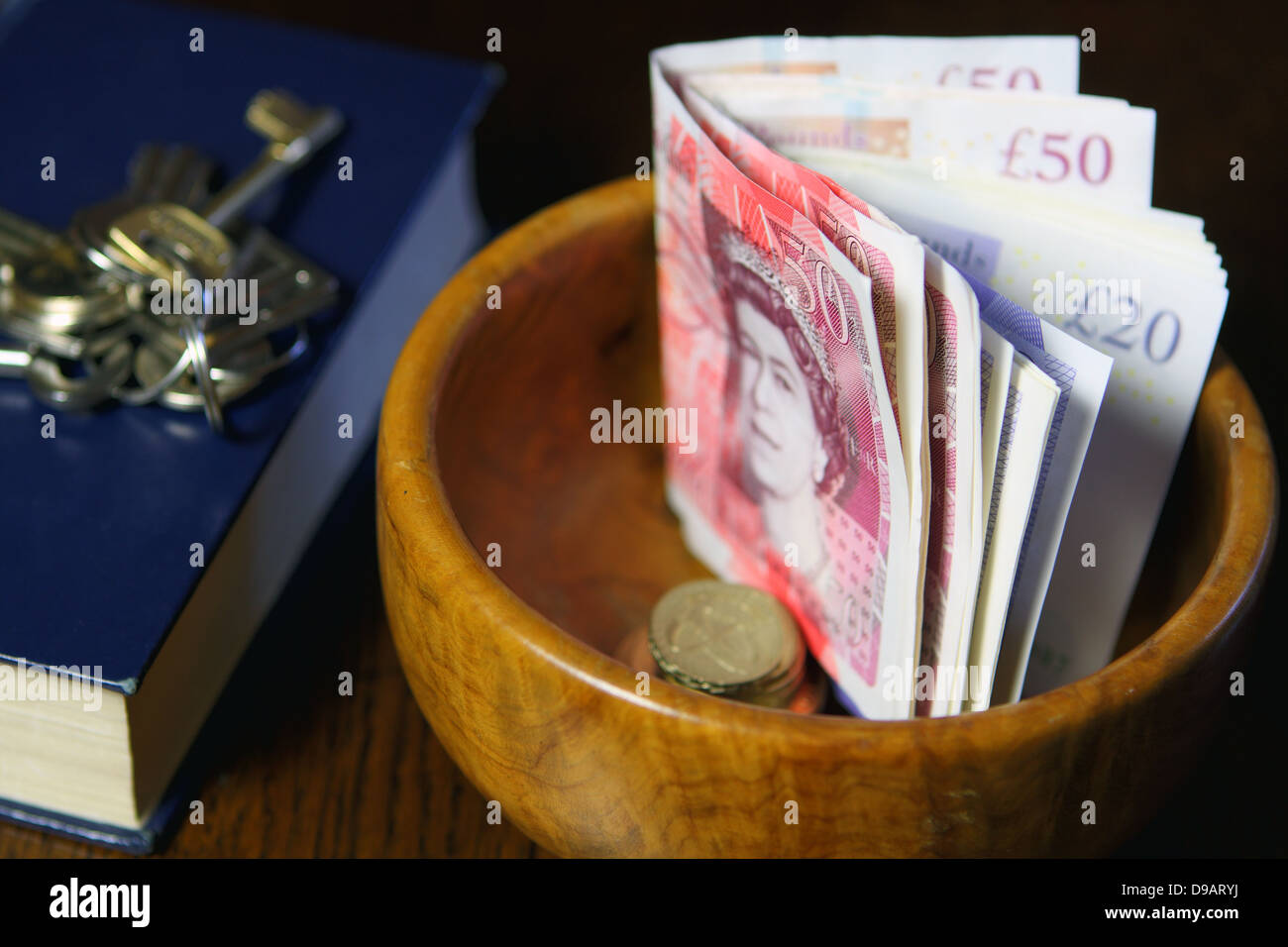 Eine braune Schale mit Sterling £50, £20 Noten- Bargelds neben Teil eines Buches mit Tasten an der Spitze Stockfoto